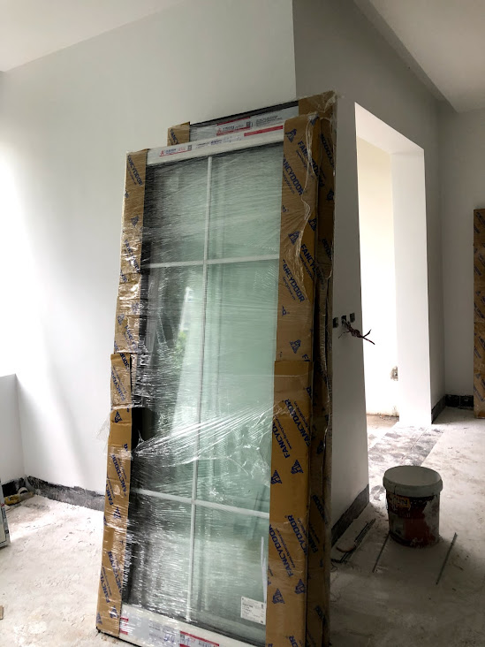 Cửa kính khung nhôm mới bọc carton và nilon đặt trong phòng đang thi công xây dựng